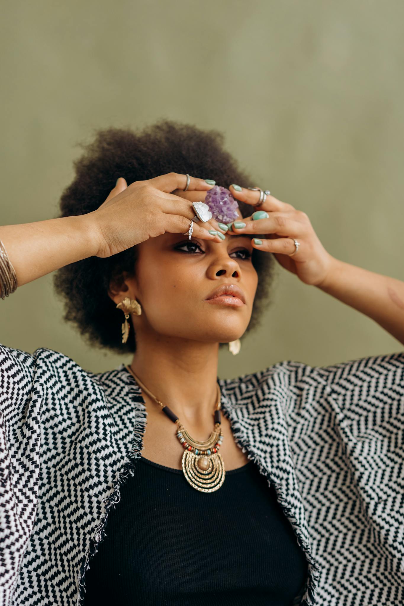 A woman practices meditation indoors, holding an amethyst crystal to her forehead for focus.