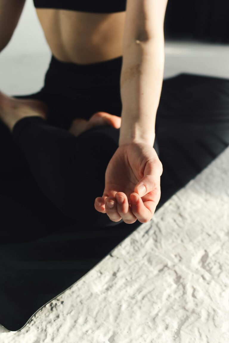 A person meditating indoors, highlighting hand posture on a yoga mat.