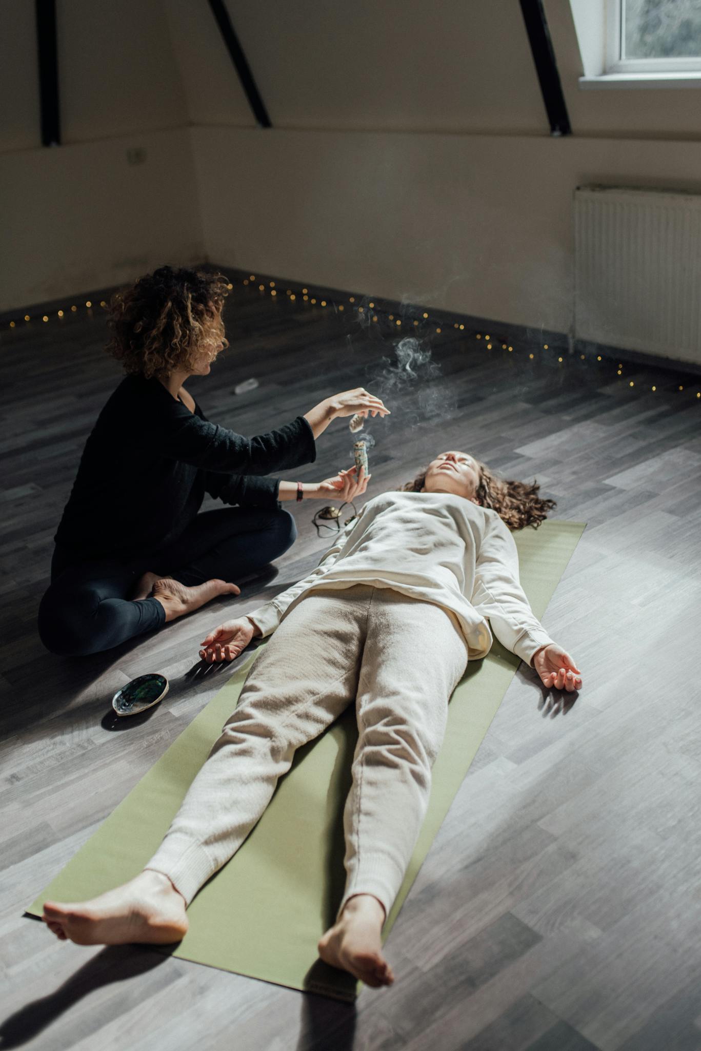 A woman lies in meditation while incense smoke creates a calming atmosphere.